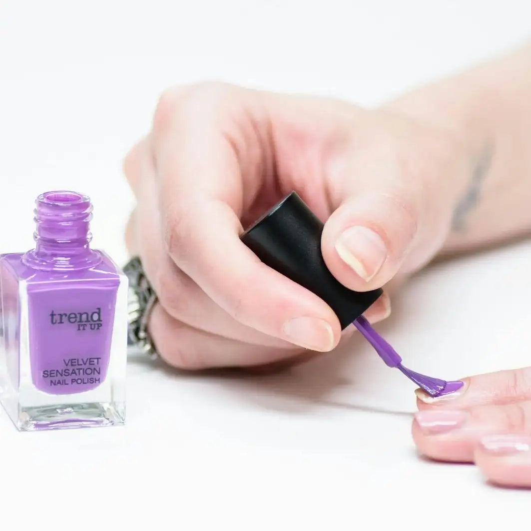 A bottle of trend it up velvet sensation nail polish in a vibrant purple hue, housed in a clear glass container with a black cap.