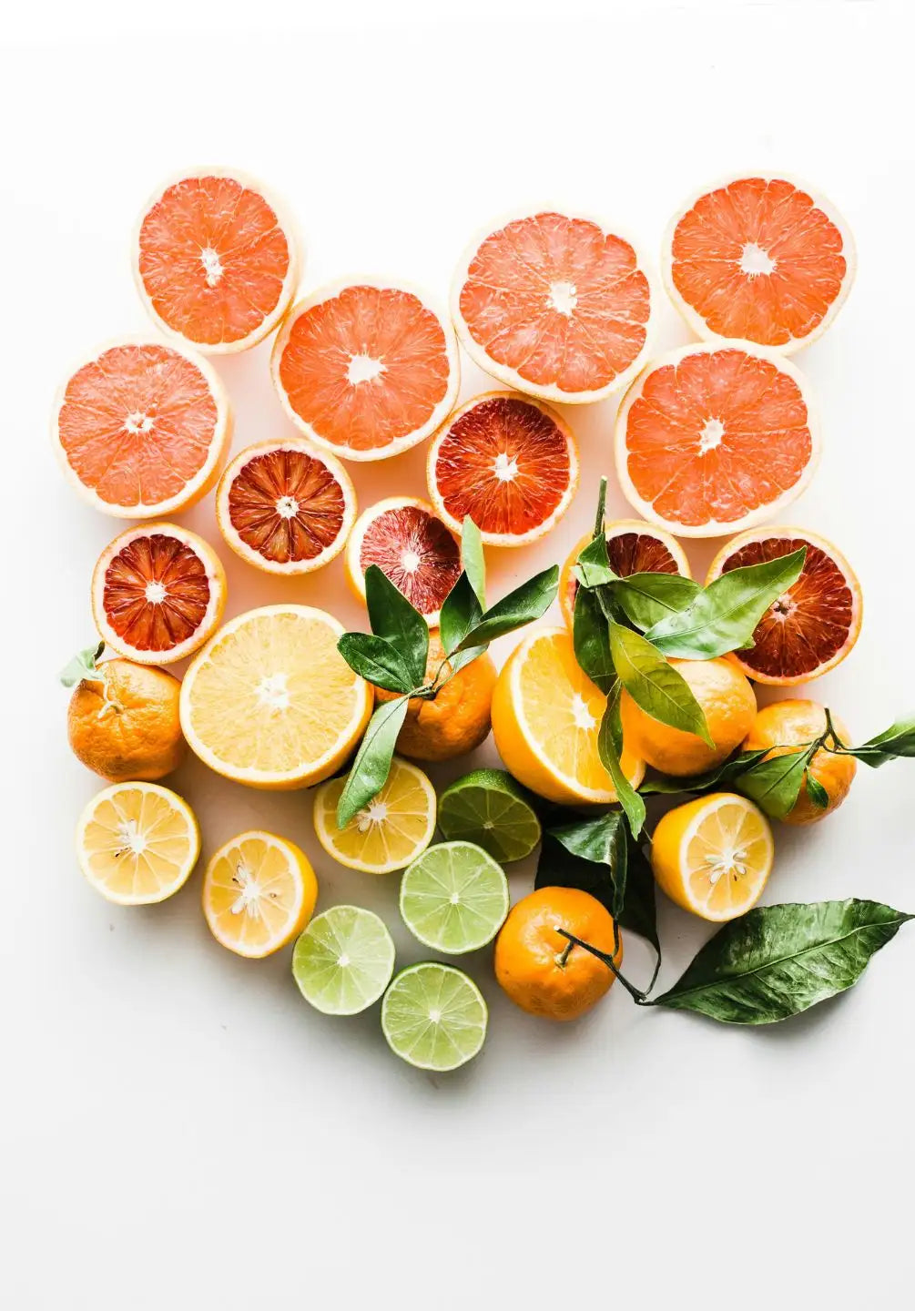 A vibrant assortment of sliced citrus fruits, including grapefruit, orange, lemon, and lime, arranged in a heart shape with fresh green leaves scattered among them.